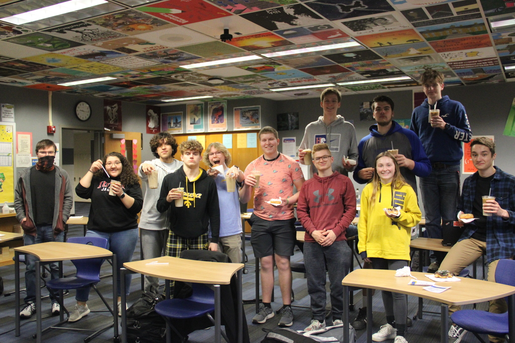 group of students in a classroom holding donuts and iced coffee
