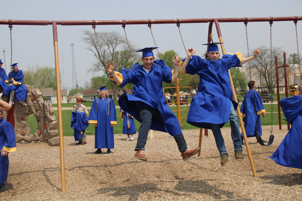 two boys jump off a swing set while wearing a graduation cap and gown